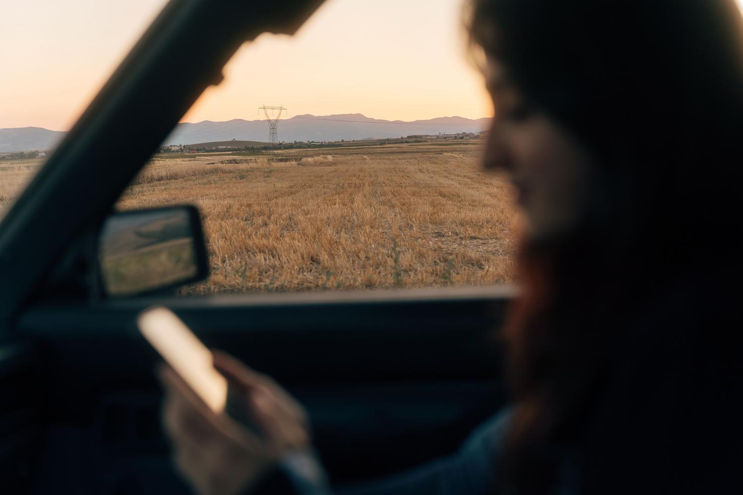 Pasajero de un coche mirando hacia el horizonte mientras sostiene su teléfono, evitando el mareo.
