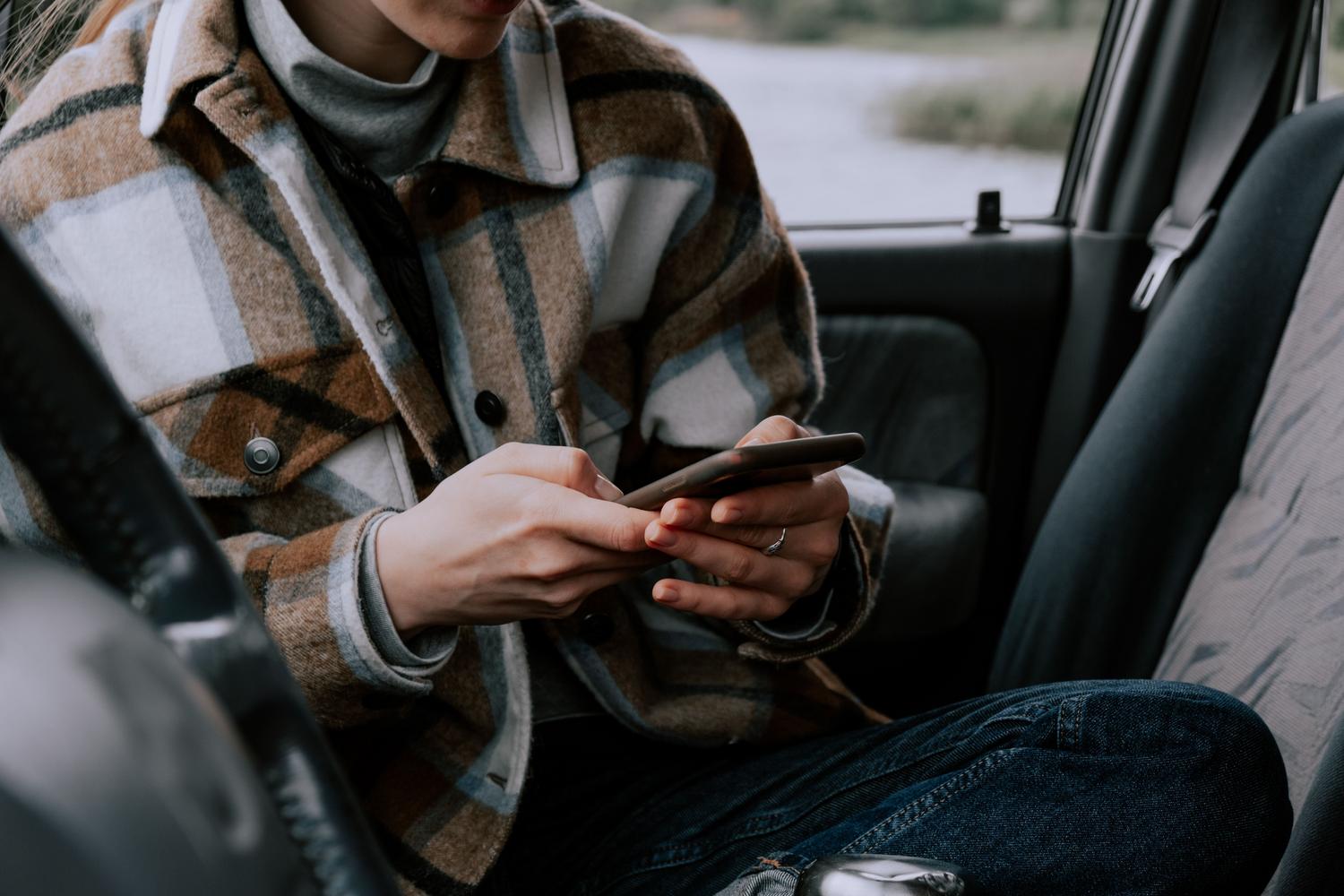 Mujer sentada en el asiento trasero de un coche usando su smartphone durante un viaje.