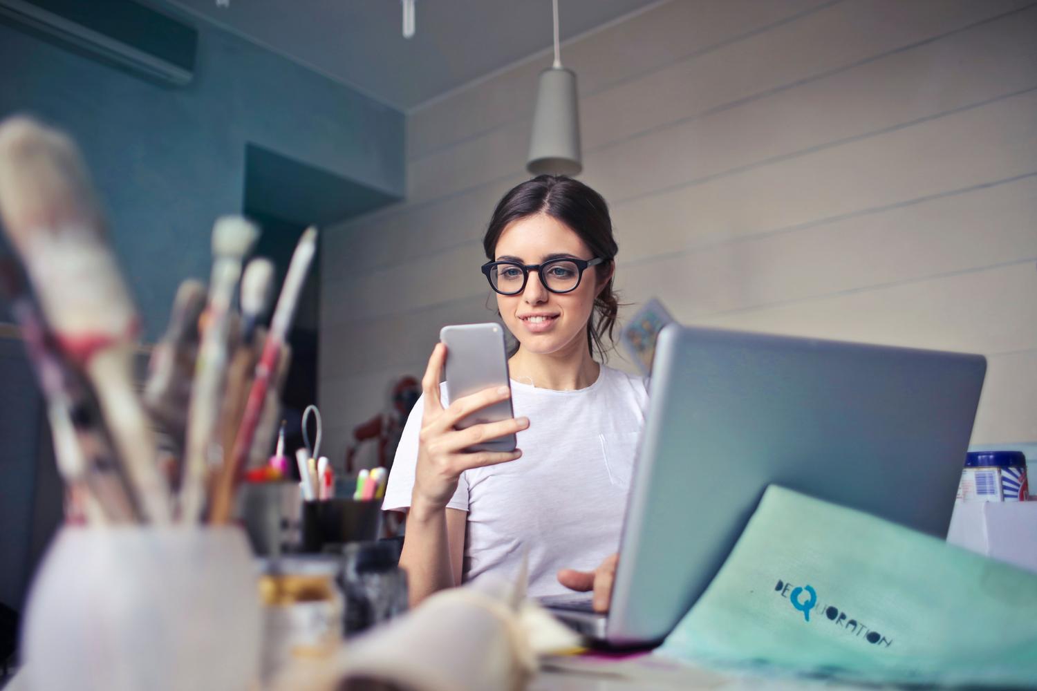 Mujer utilizando un smartphone y un ordenador portátil para gestionar por separado sus actividades personales y profesionales.