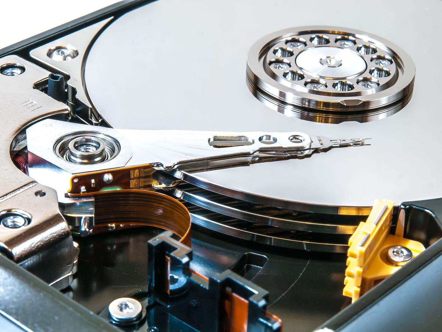 Vista detallada del interior de un disco duro mecánico (HDD), mostrando los platos y el brazo lector, donde ocurre el cuello de botella del 100% de uso.