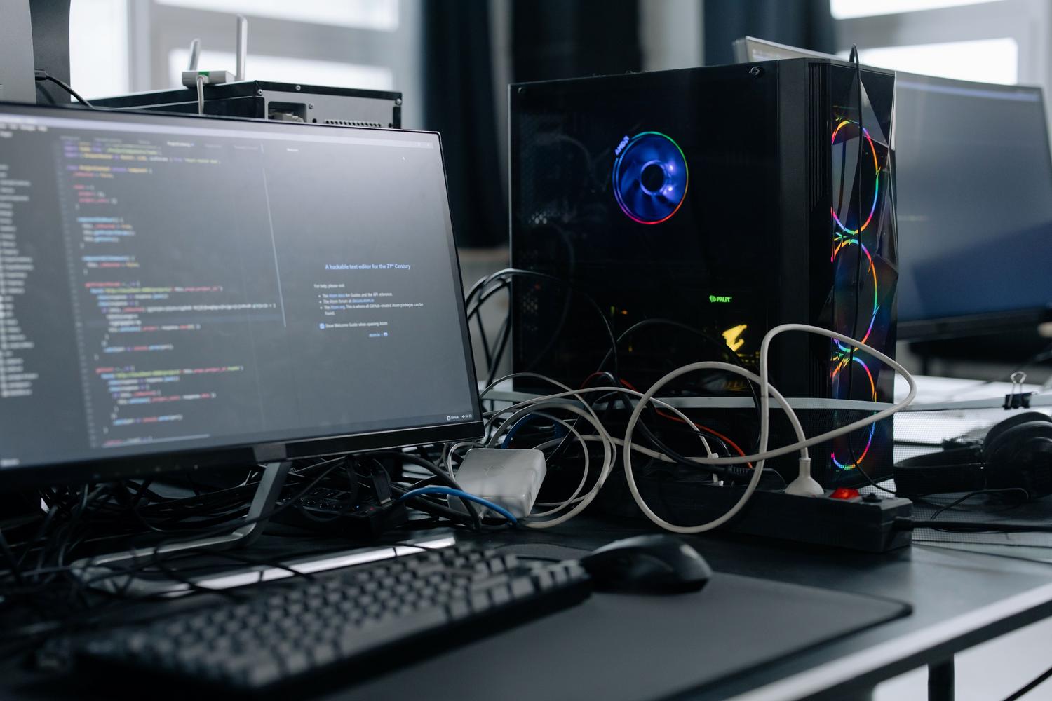 Estación de trabajo moderna con monitor de código y torre de PC de alto rendimiento con iluminación RGB.