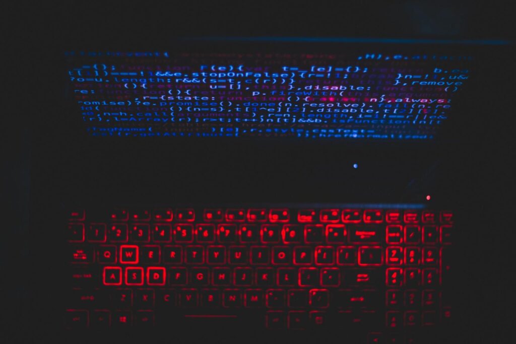Configuración de laptop con teclado retroiluminado en rojo y código en pantalla, ideal para representar procesos de sistema.