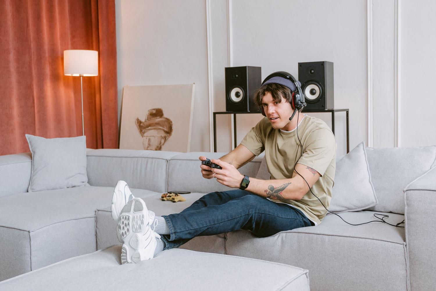Young man sitting on a sofa enjoying a video game session at home with headphones