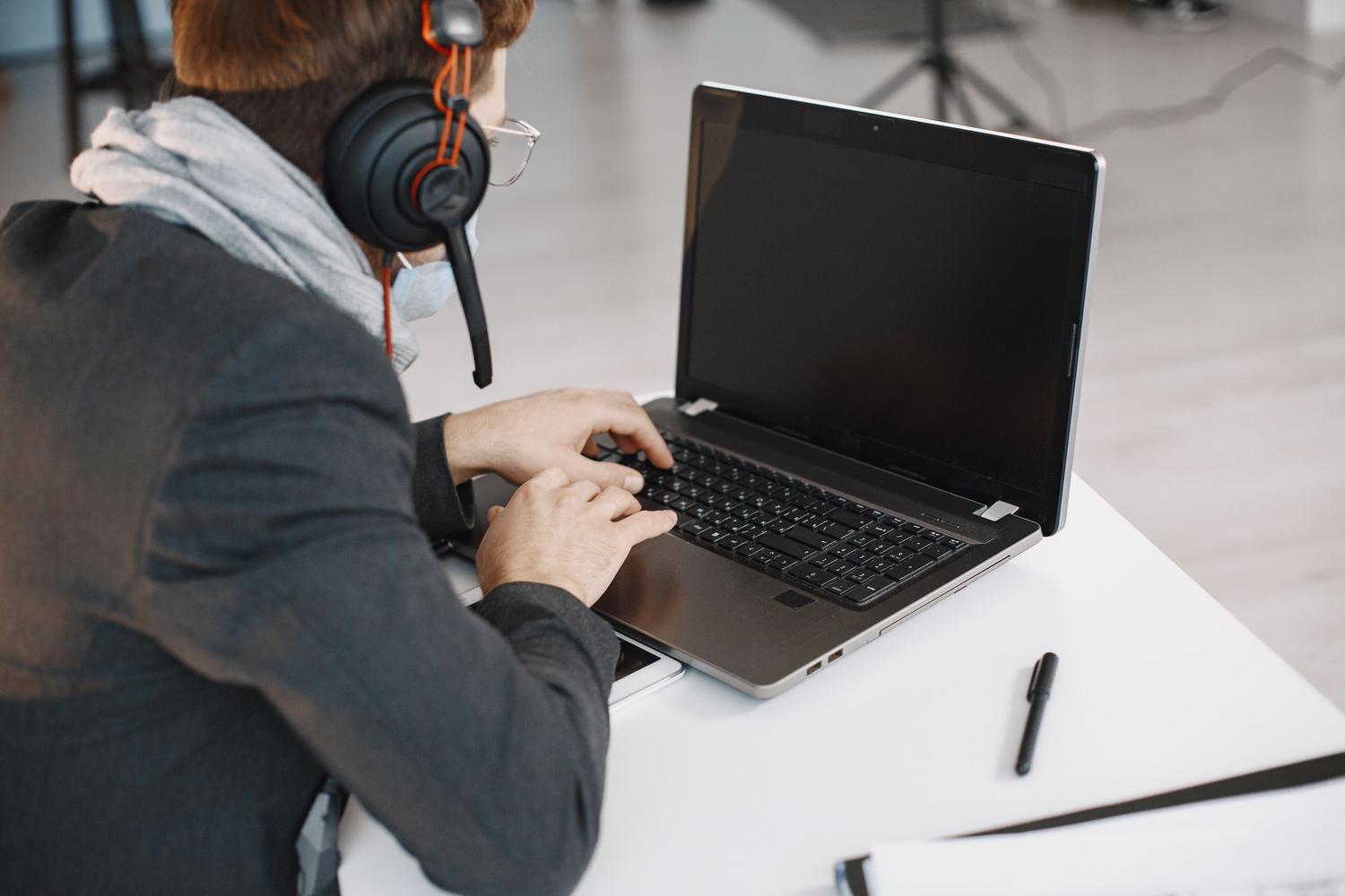 Hombre participando en una videollamada con auriculares y un ordenador portátil.