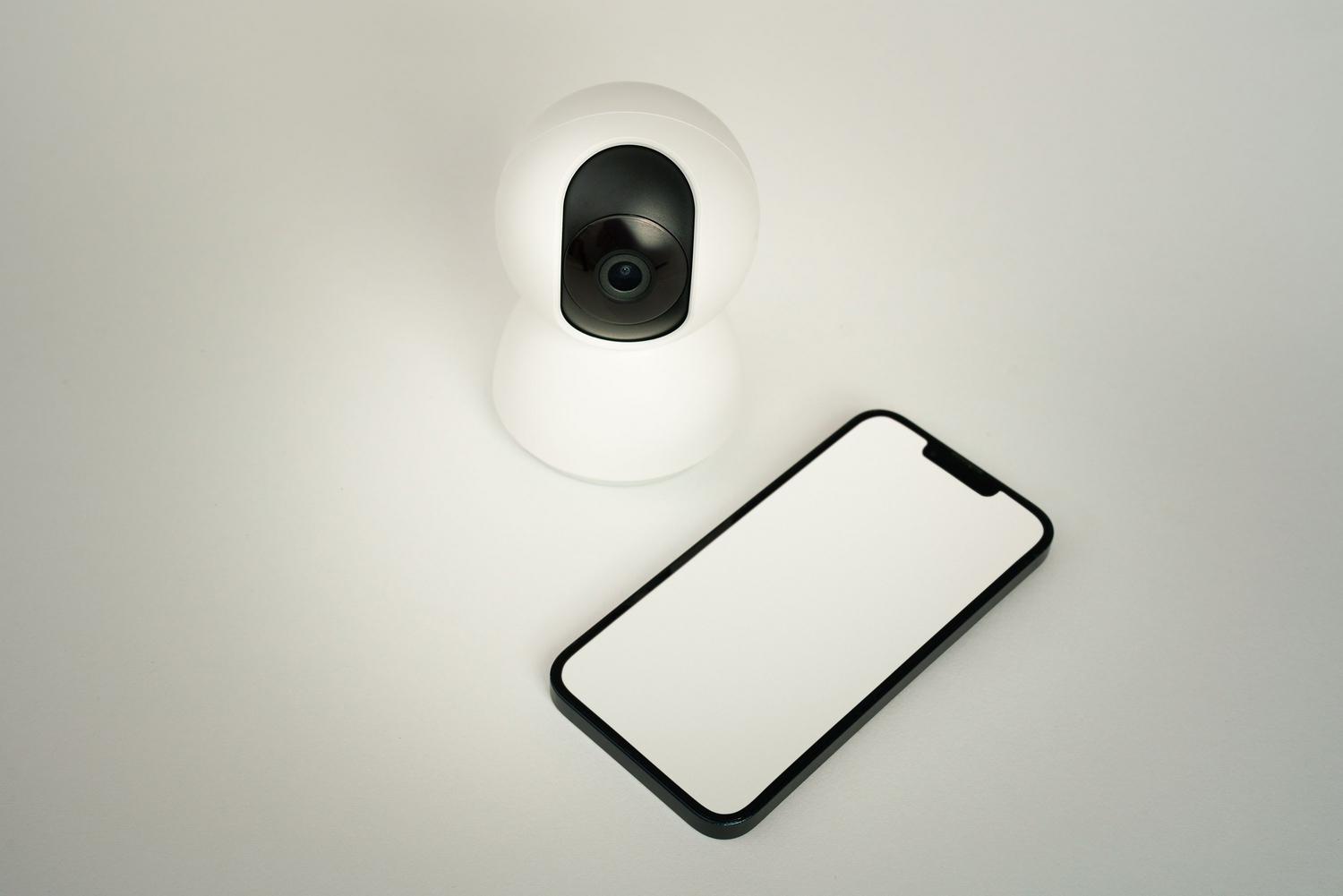 Cámara de seguridad inteligente junto a un teléfono móvil, representando la recepción de notificaciones y alertas.