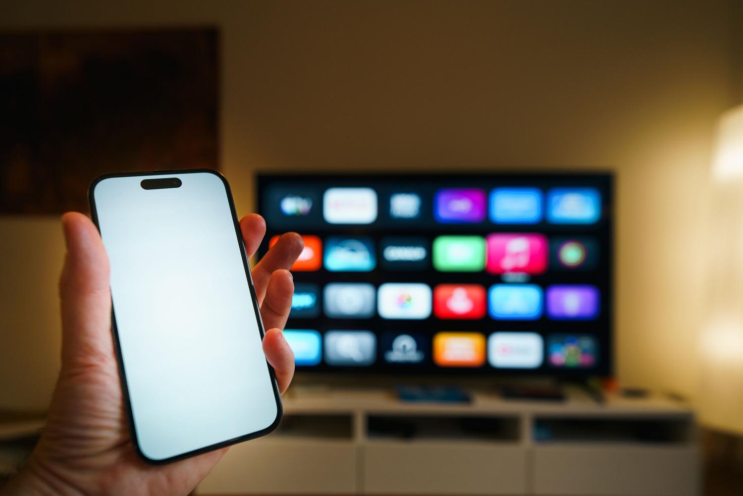 Smartphone situado frente a un televisor, representando la integración de Apple Music y Apple Podcasts en el ecosistema de Apple.