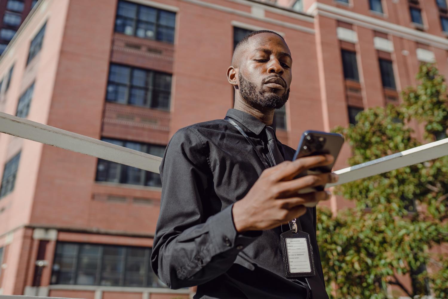 Hombre de negocios utilizando su teléfono móvil en un entorno corporativo urbano, representando la movilidad y el acceso remoto a documentos empresariales.