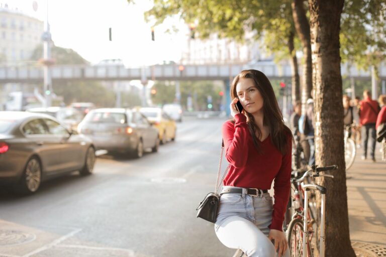 Mujer con suéter rojo hablando por teléfono en una calle con tráfico intenso, representando el ruido urbano.