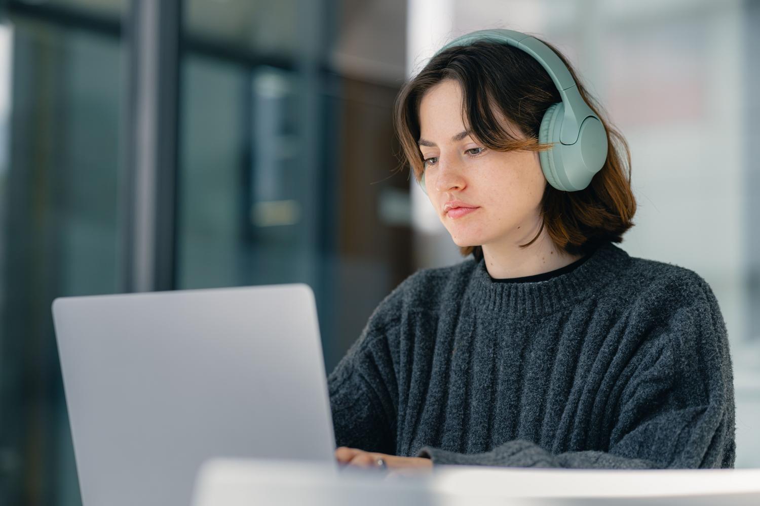 Persona escuchando con auriculares el contenido de un PDF abierto en un portátil