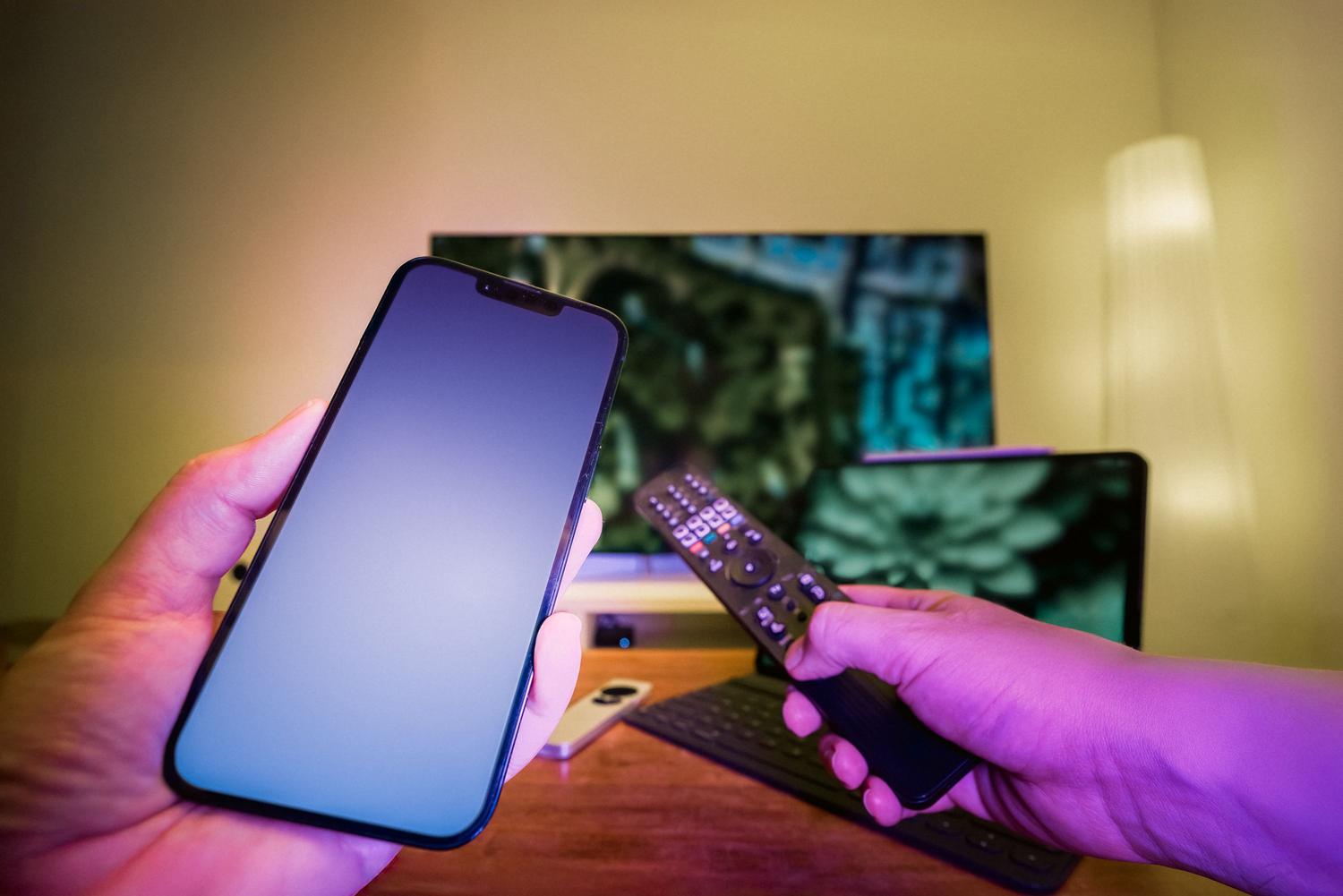 Usuario utilizando un mando y un teléfono para configurar las conexiones de una Smart TV.