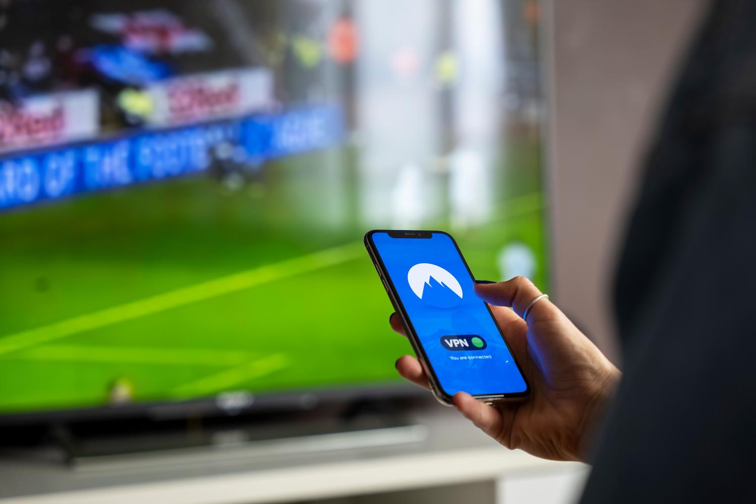 Persona utilizando un smartphone junto a una televisión.