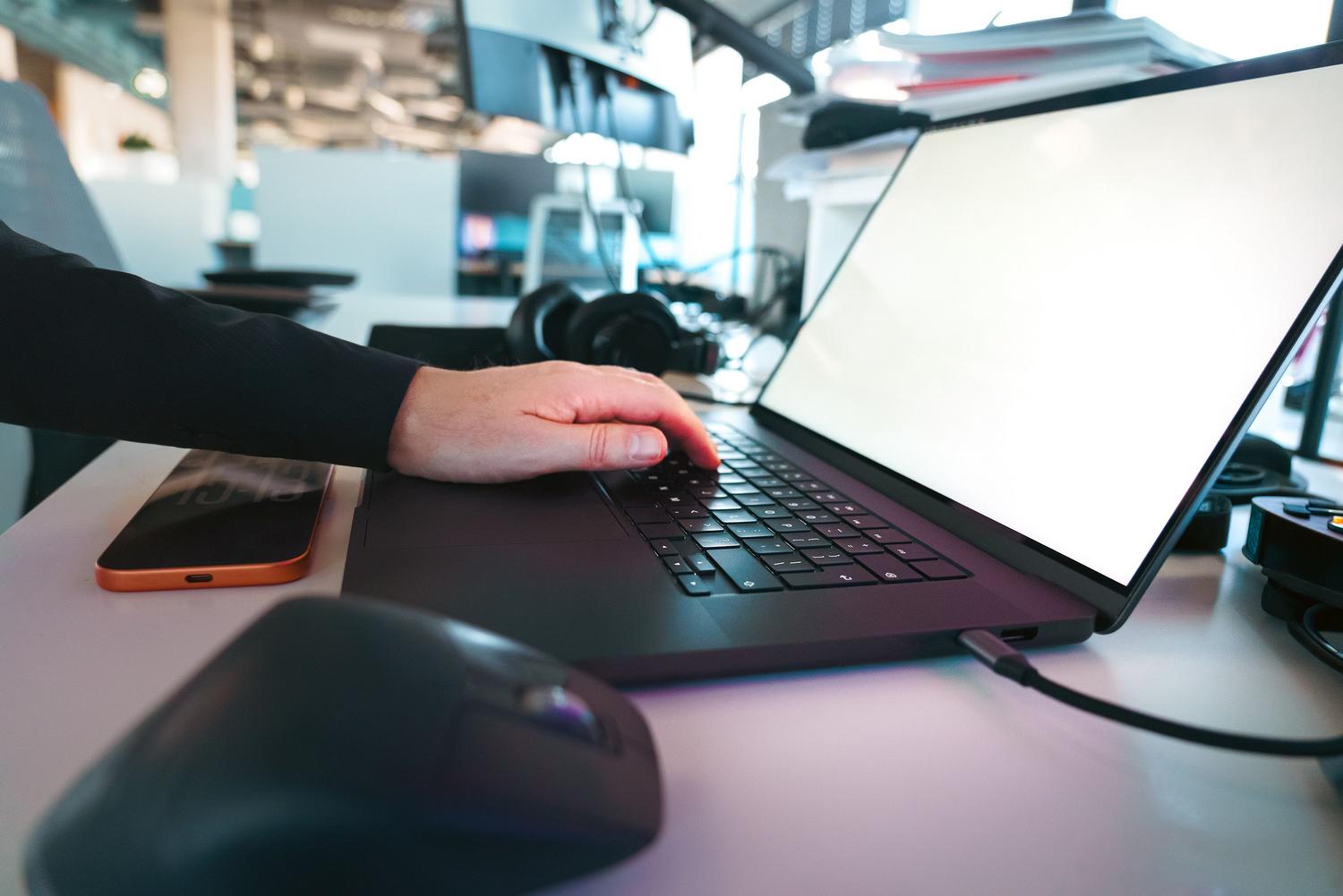 Primer plano de manos utilizando un teclado de portátil en una oficina moderna, ideal para representar atajos de teclado
