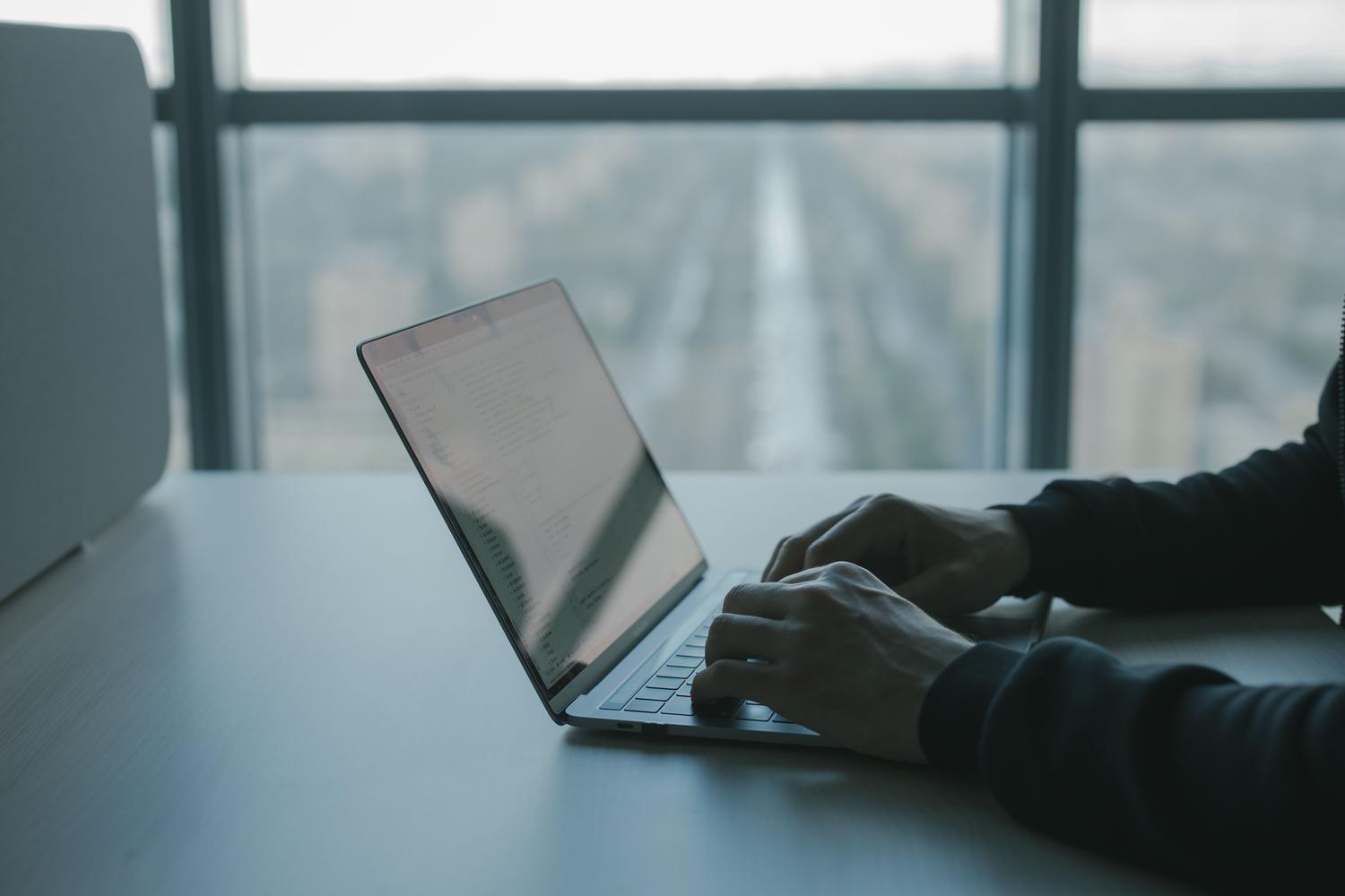 Persona concentrada escribiendo en un portátil en un entorno de oficina moderno y luminoso