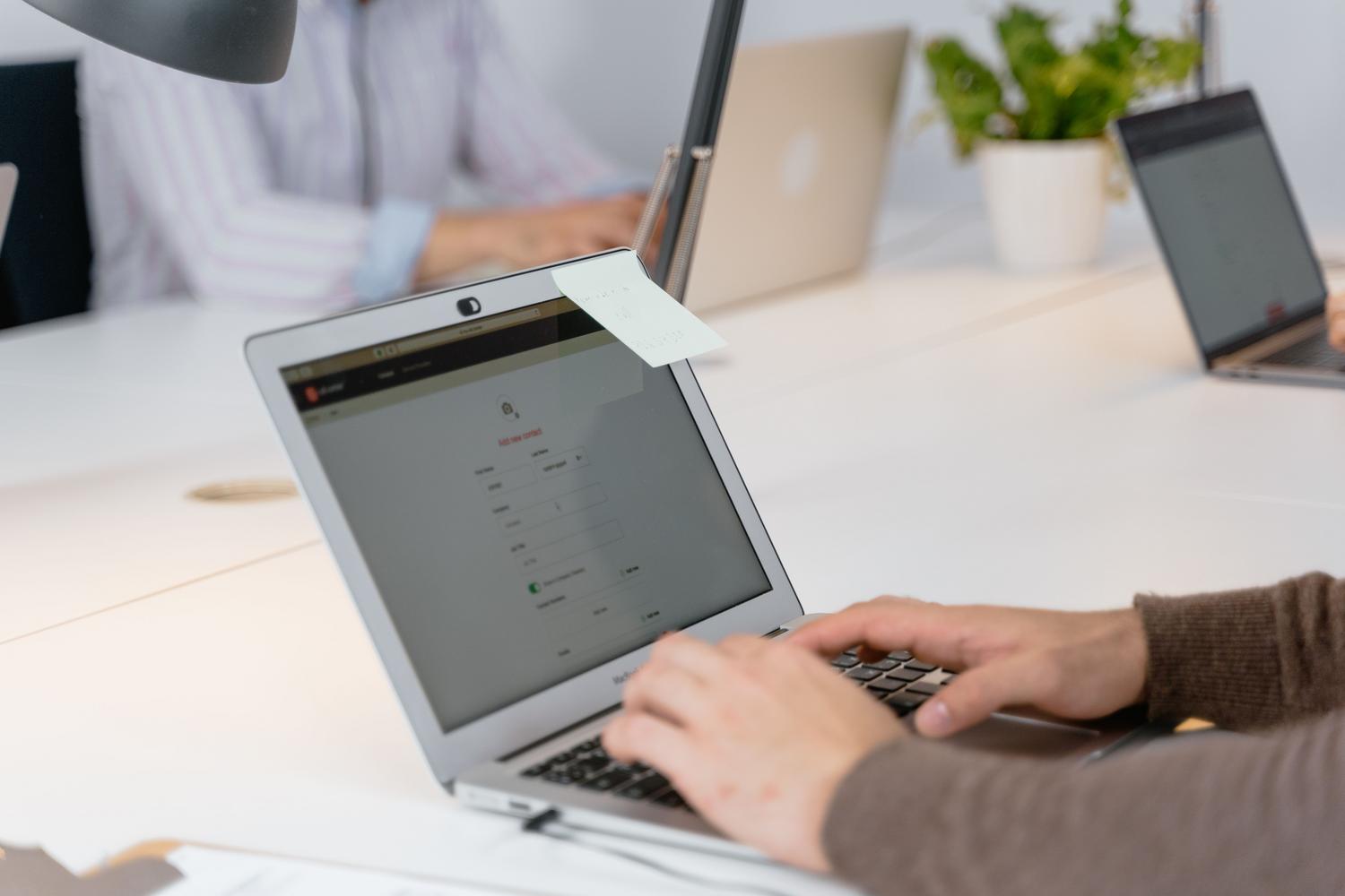 Primer plano de una persona trabajando en un portátil con una nota adhesiva amarilla en la pantalla para recordar tareas