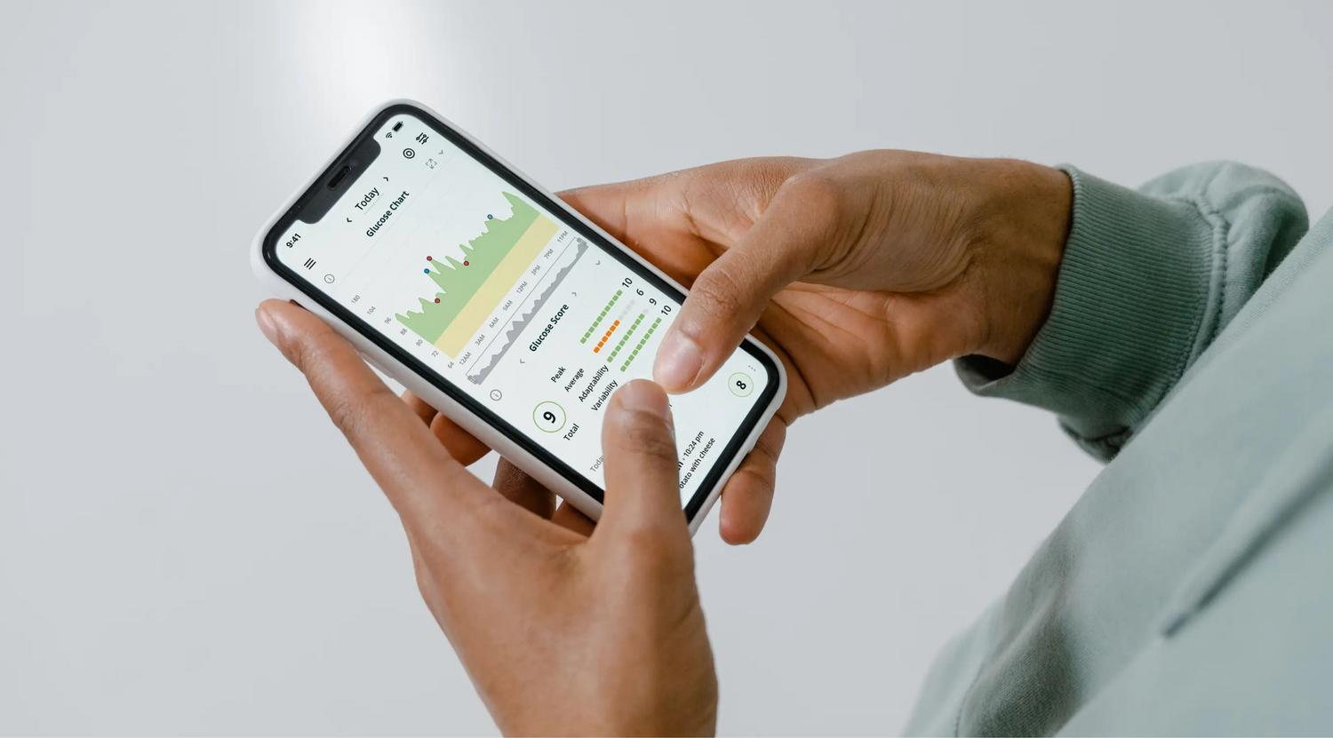 Primer plano de manos sosteniendo un smartphone con una aplicación de seguimiento de salud y gráficos de datos analíticos.