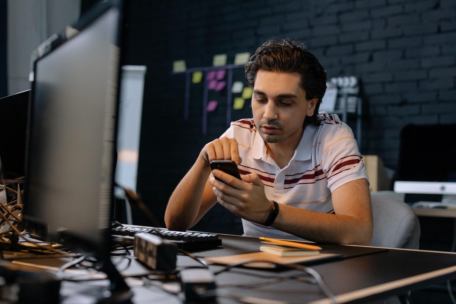 Joven profesional concentrado utilizando su smartphone en un escritorio de oficina minimalista.