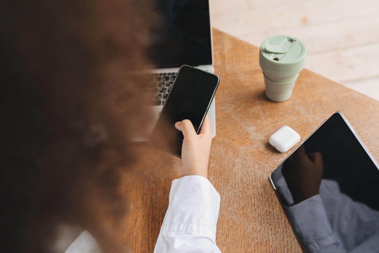 Vista cenital de una persona organizando su espacio de trabajo con dispositivos electrónicos y café, simbolizando la gestión de tareas.