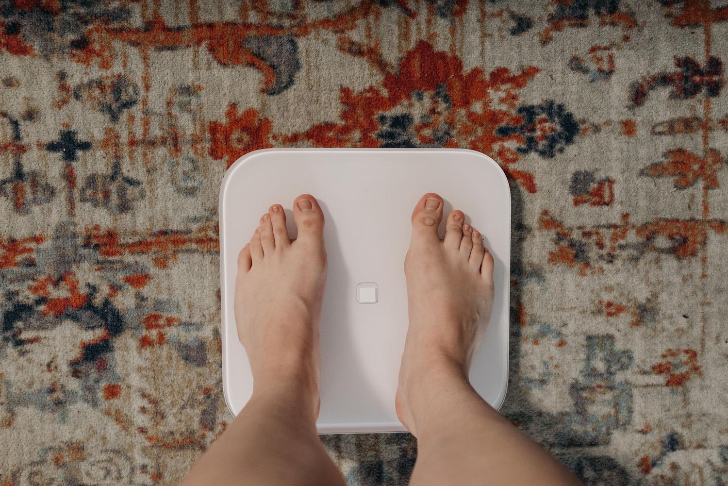 Vista cenital de unos pies sobre una báscula inteligente en el baño, representando la configuración de una Fitbit Aria.