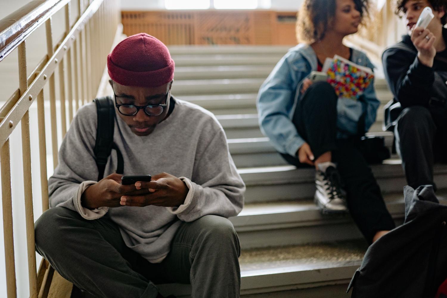 Estudiantes relajados en el campus revisando sus teléfonos móviles durante un descanso.