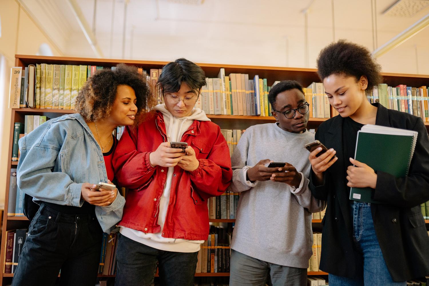 Jóvenes universitarios utilizando sus móviles en una biblioteca, integrando la tecnología en el entorno académico.