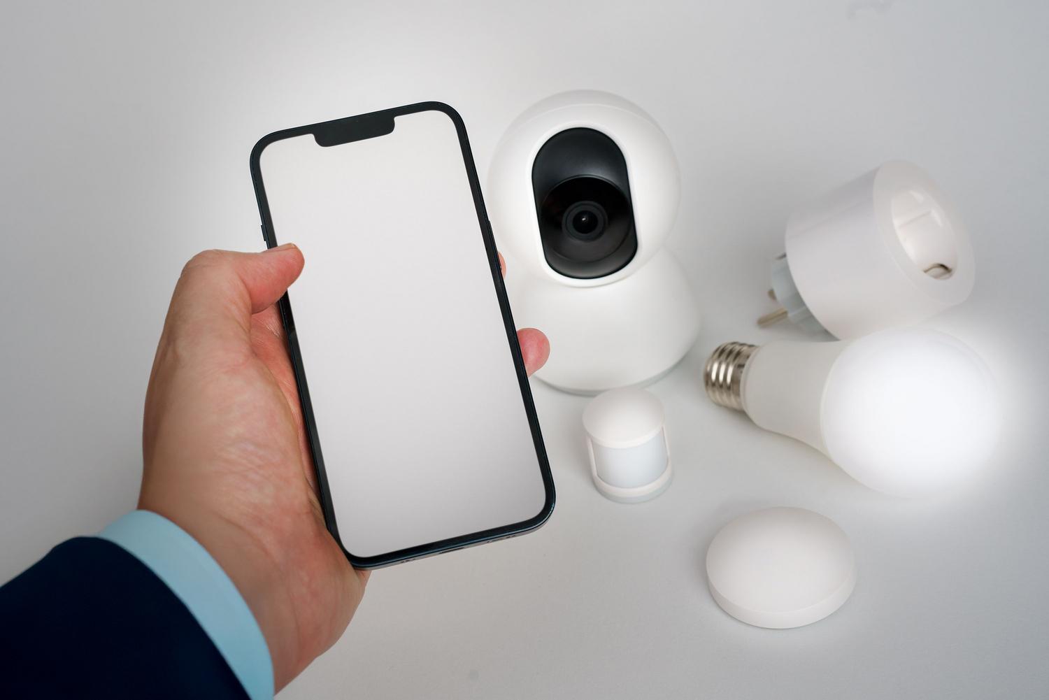Conjunto de dispositivos de hogar inteligente, incluyendo cámara y bombillas, controlados centralmente desde la pantalla de un smartphone.
