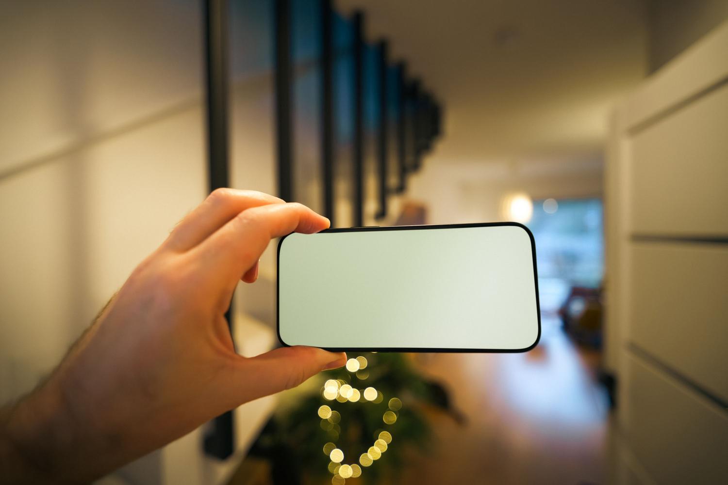 Persona sosteniendo un smartphone con una sola mano en el interior de una casa moderna, ilustrando el control accesible de SmartThings.