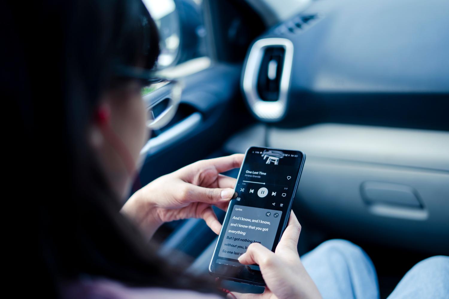 Persona en el interior de un vehículo utilizando el móvil para consumir audio durante un trayecto