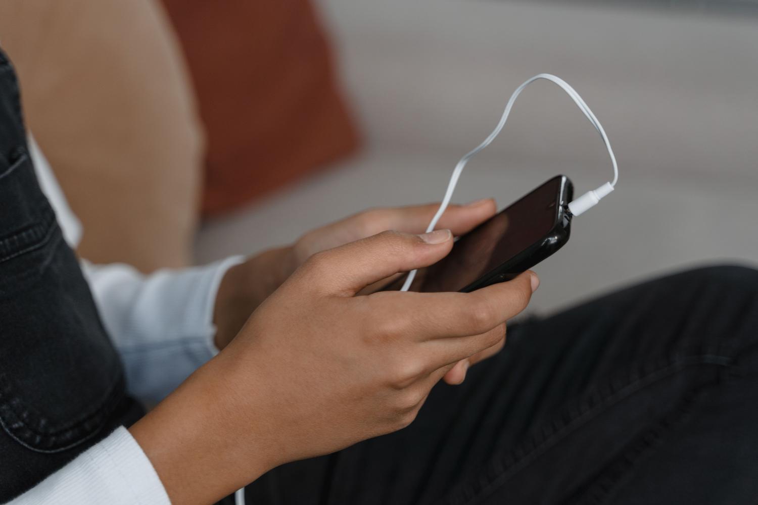 Primer plano de manos sosteniendo un smartphone con auriculares conectados, representando la escucha de contenido digital