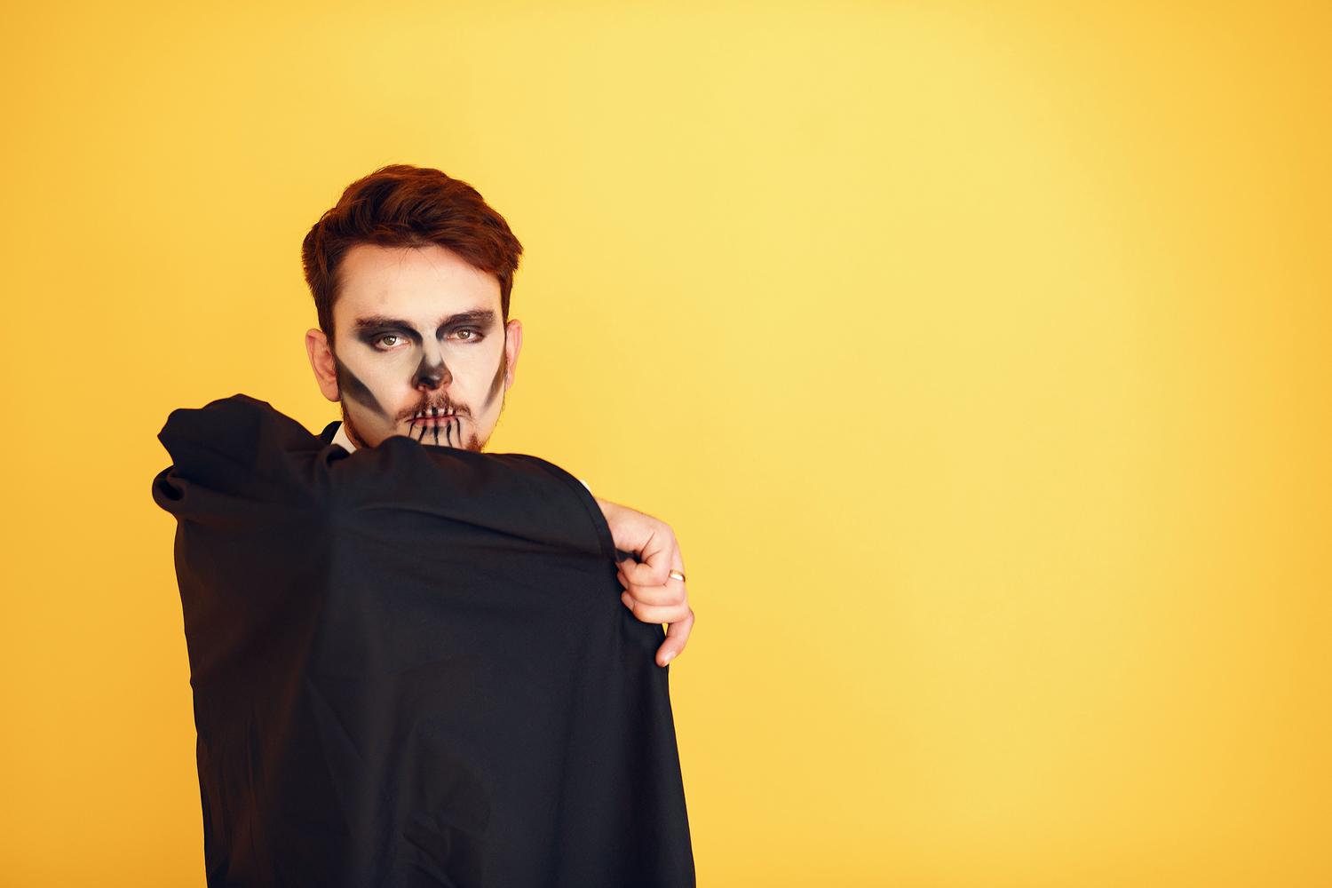 Männerporträt mit Totenkopf-Make-up und schwarzem Anzug vor leuchtend gelbem Hintergrund.