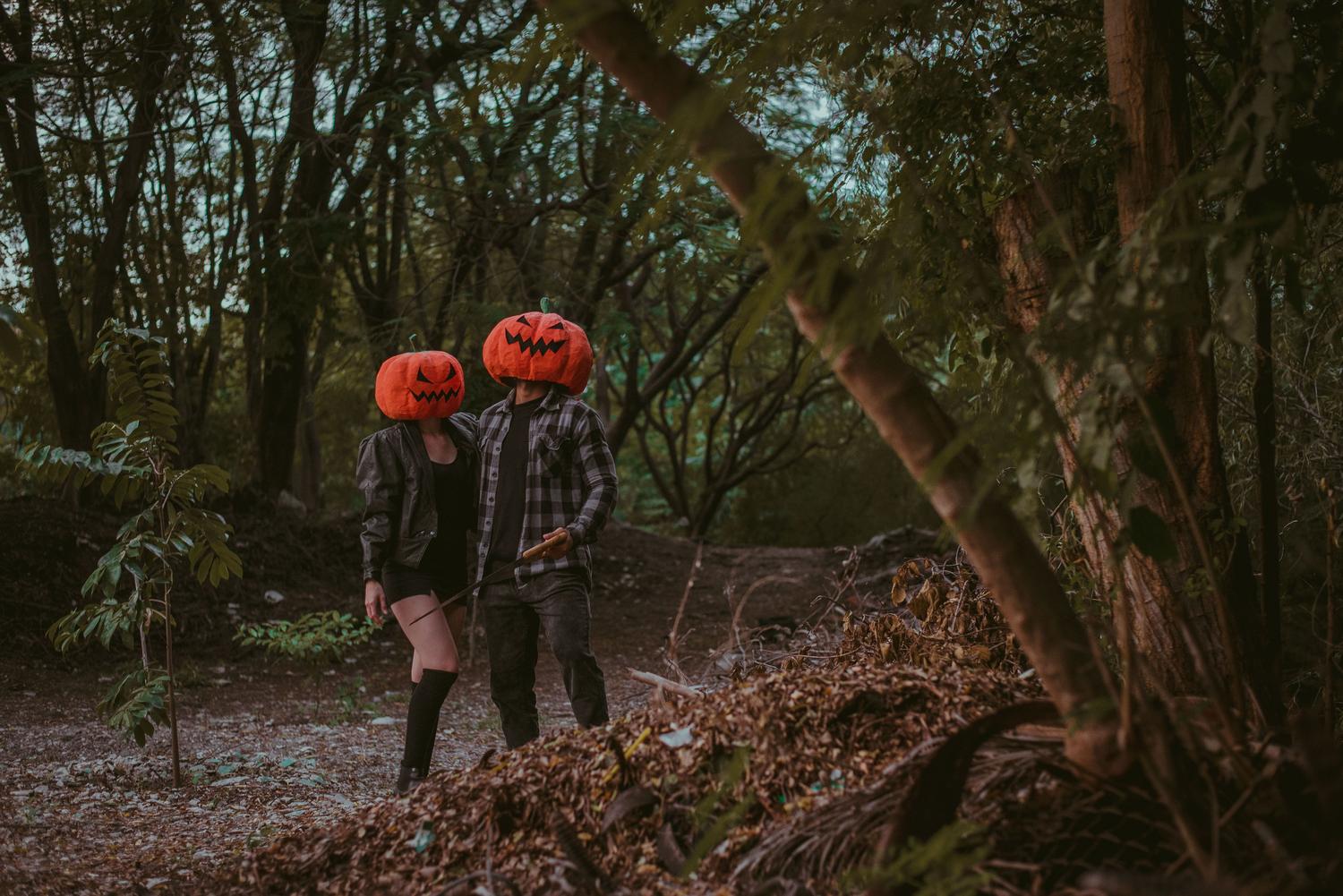Pareja con máscaras de calabaza en un bosque oscuro y neblinoso, ideal para ilustrar fondos de terror generados por IA.