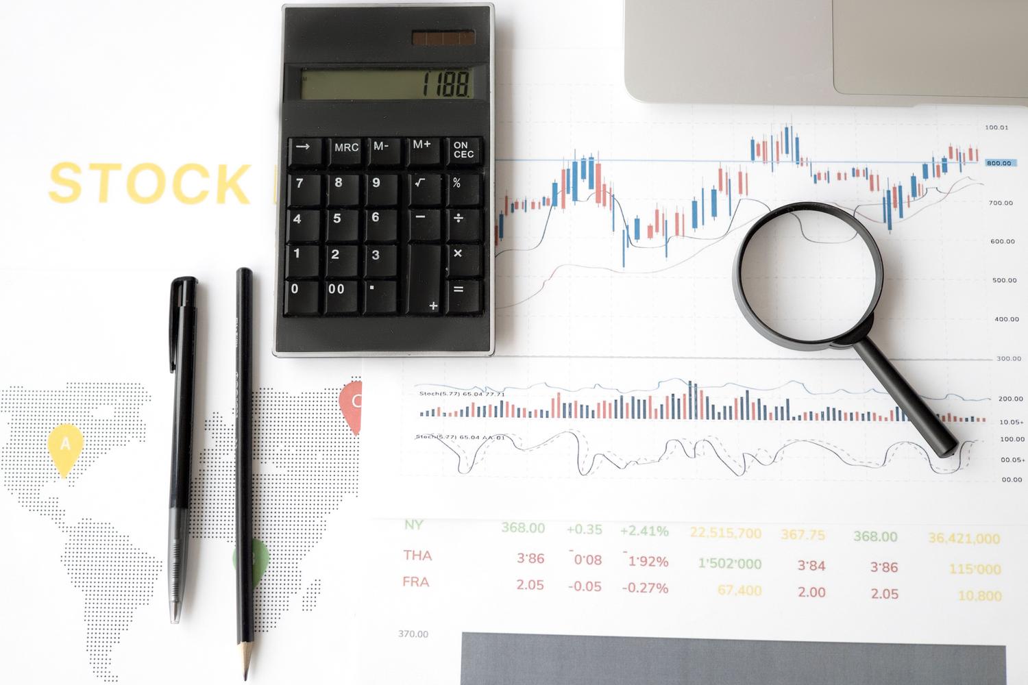 Conjunto de herramientas de análisis financiero con calculadora, gráficos de velas y lupa sobre un fondo blanco.