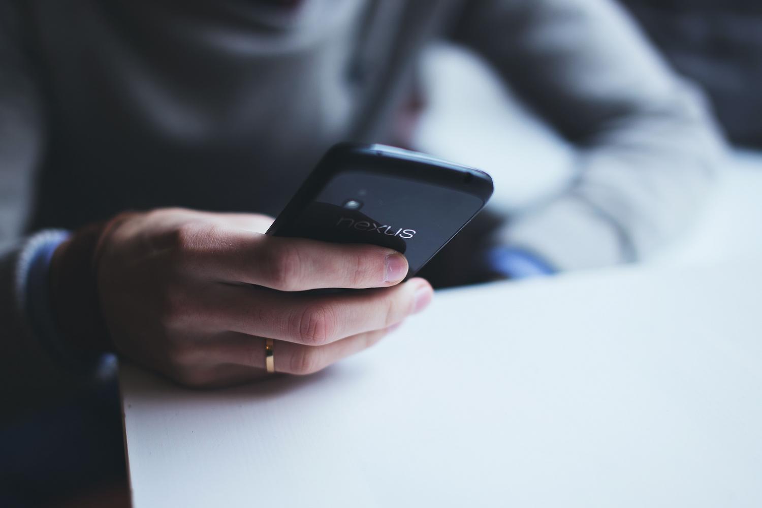 Detalle de una persona sosteniendo un smartphone sobre una mesa, simulando la navegación por internet.