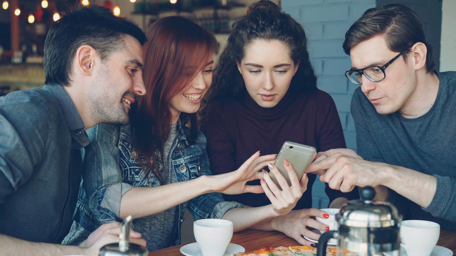Amigos compartiendo un momento social y revisando imágenes en sus dispositivos móviles mientras toman café.