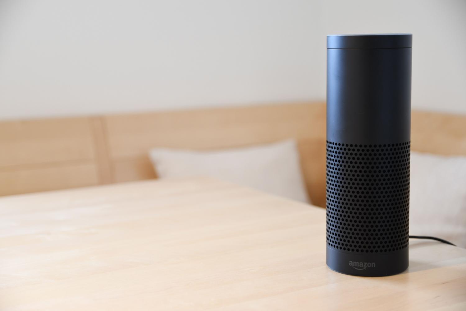 Un altavoz inteligente Amazon Echo negro sobre una mesa de madera en un ambiente hogareño.