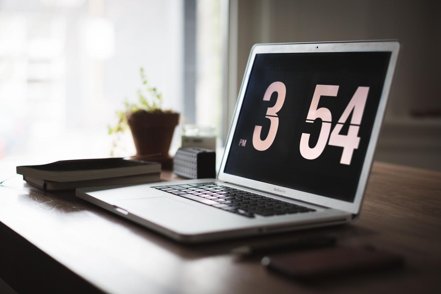 Espacio de trabajo moderno con laptop y reloj, ilustrando la gestión eficiente del tiempo y la productividad en la oficina.