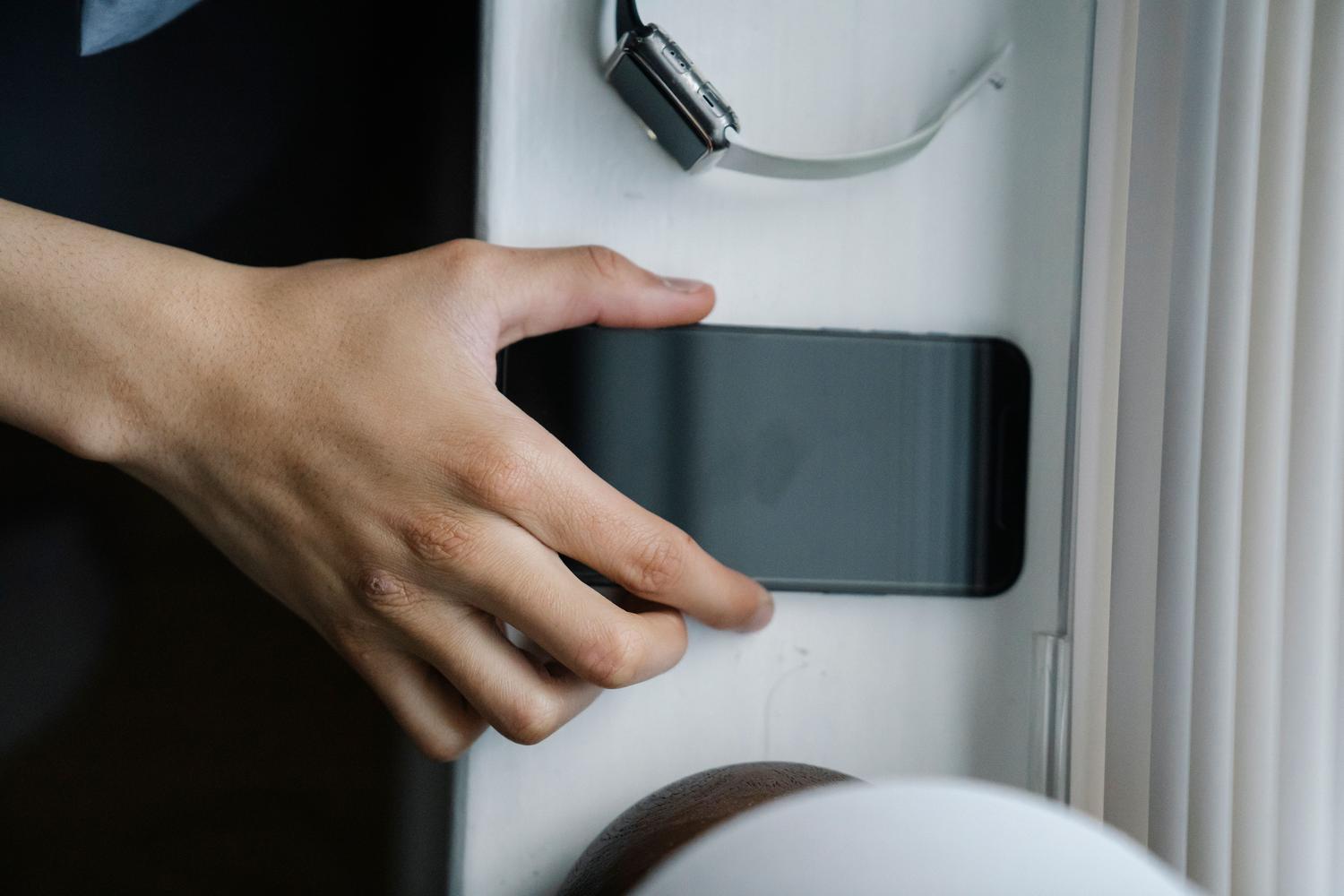 Mano recogiendo un teléfono móvil de una superficie blanca, representando el momento de encontrar el dispositivo.