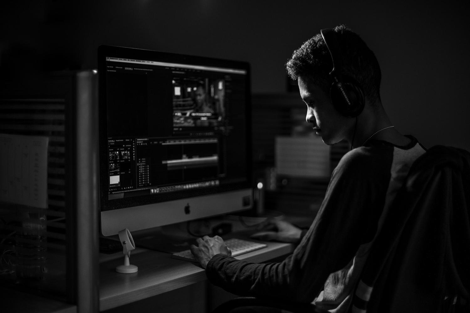 Editor de vídeo profesional trabajando con auriculares en un estudio con iluminación tenue y un monitor Apple.