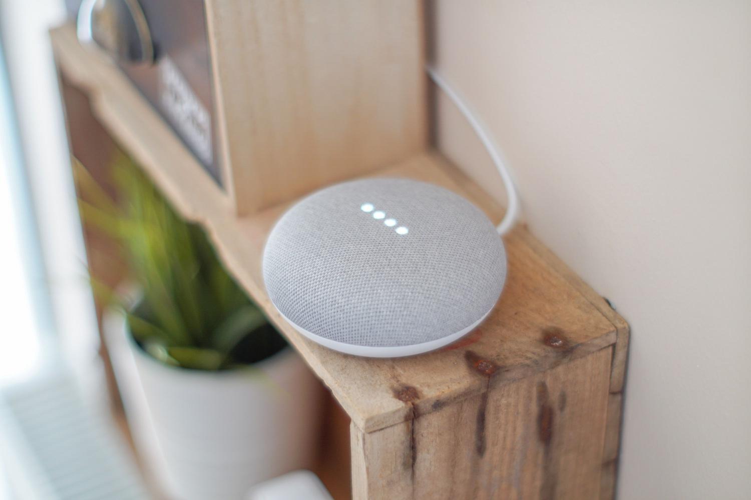 Altavoz inteligente Google Home Mini de color gris sobre un estante de madera.