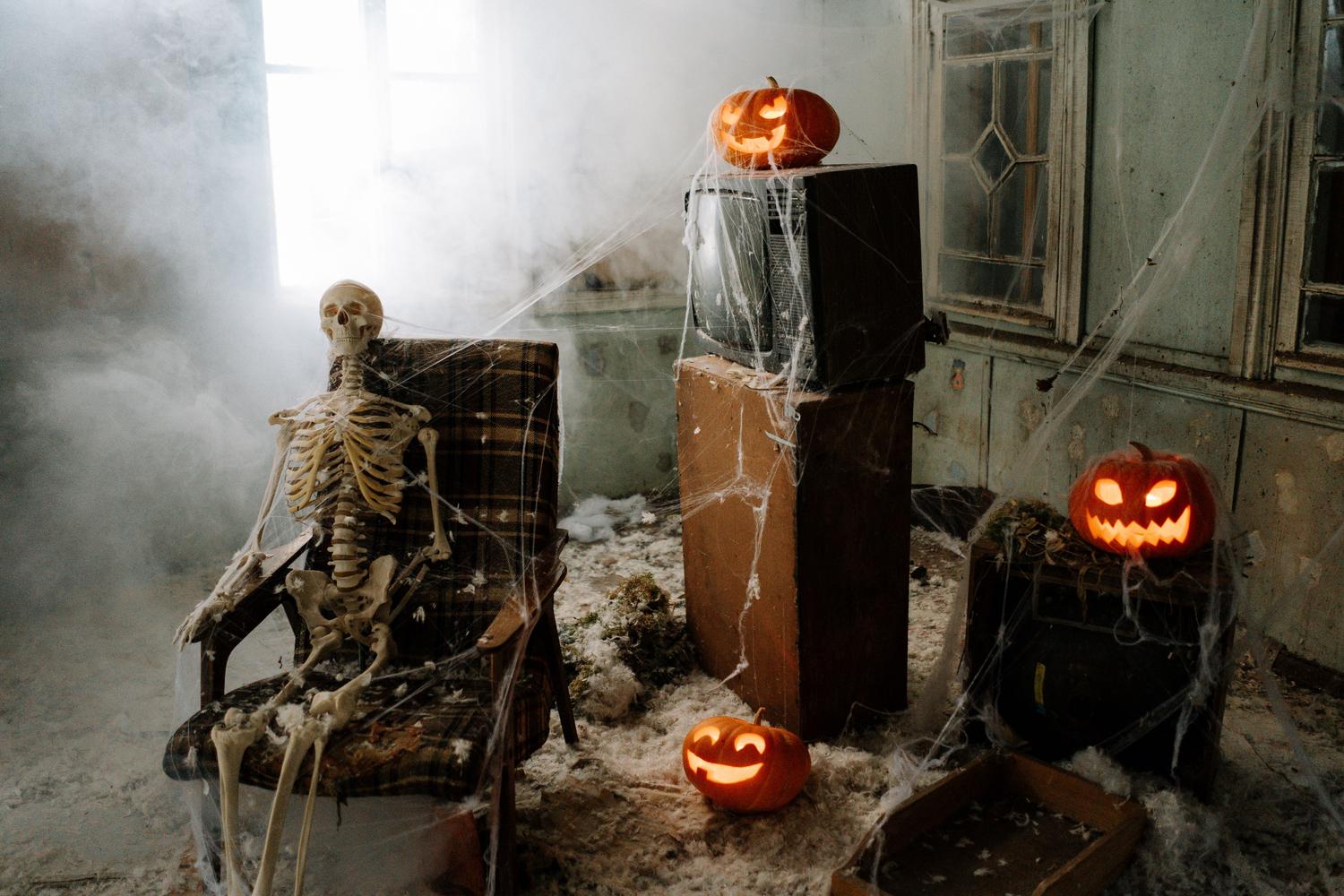 Sala de estar decorada para Halloween con un esqueleto en un sillón, calabazas iluminadas y niebla, creando una atmósfera espeluznante.