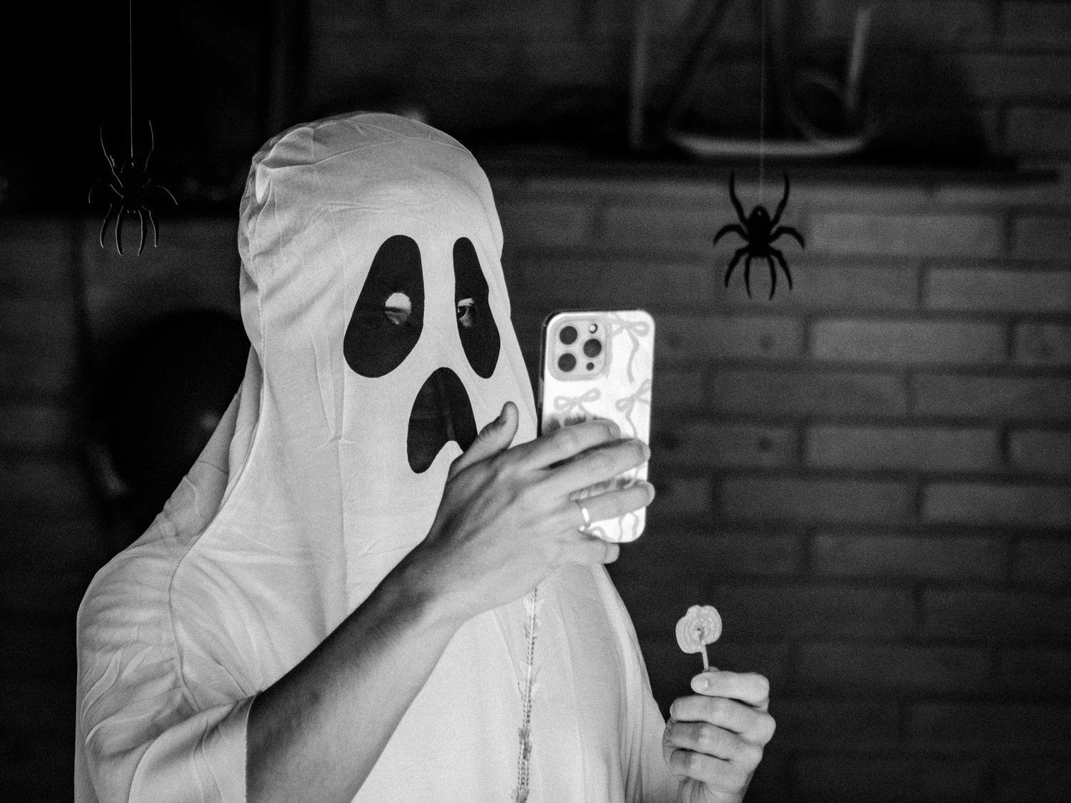 Una persona disfrazada de fantasma tomándose una selfie con un iPhone, capturando el espíritu divertido de la temporada.