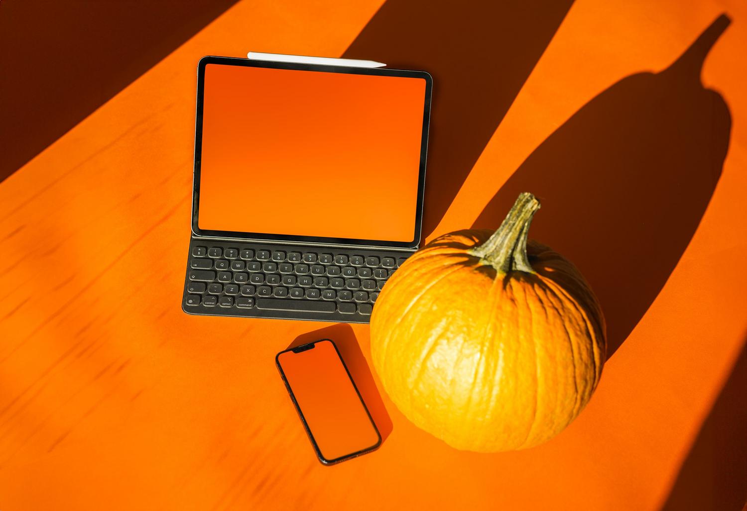 Decoración de otoño con una calabaza junto a un portátil y un smartphone, ideal para ambientar el espacio de trabajo en Halloween.