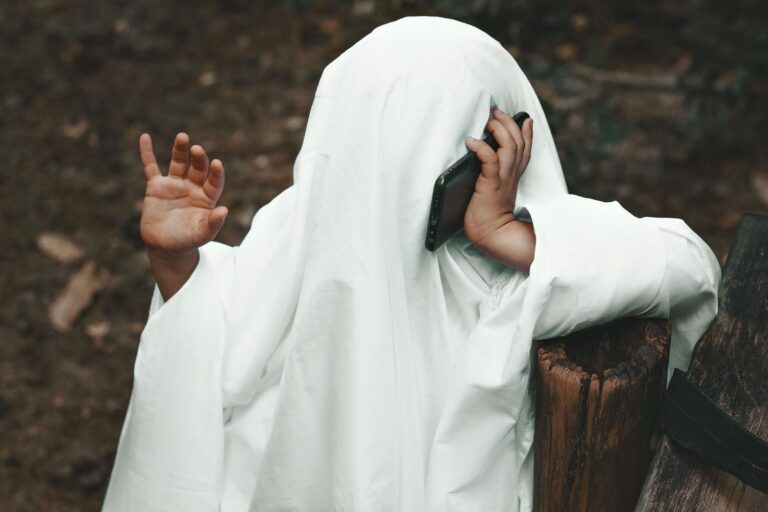 Persona disfrazada de fantasma realizando una llamada telefónica en un entorno otoñal, ideal para ilustrar la temática de tonos de Halloween.