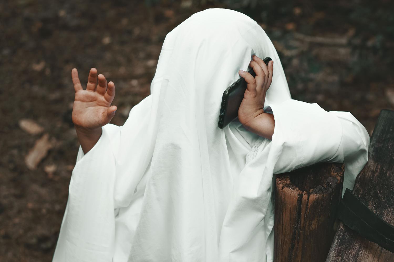 Persona disfrazada de fantasma realizando una llamada telefónica en un entorno otoñal, ideal para ilustrar la temática de tonos de Halloween.