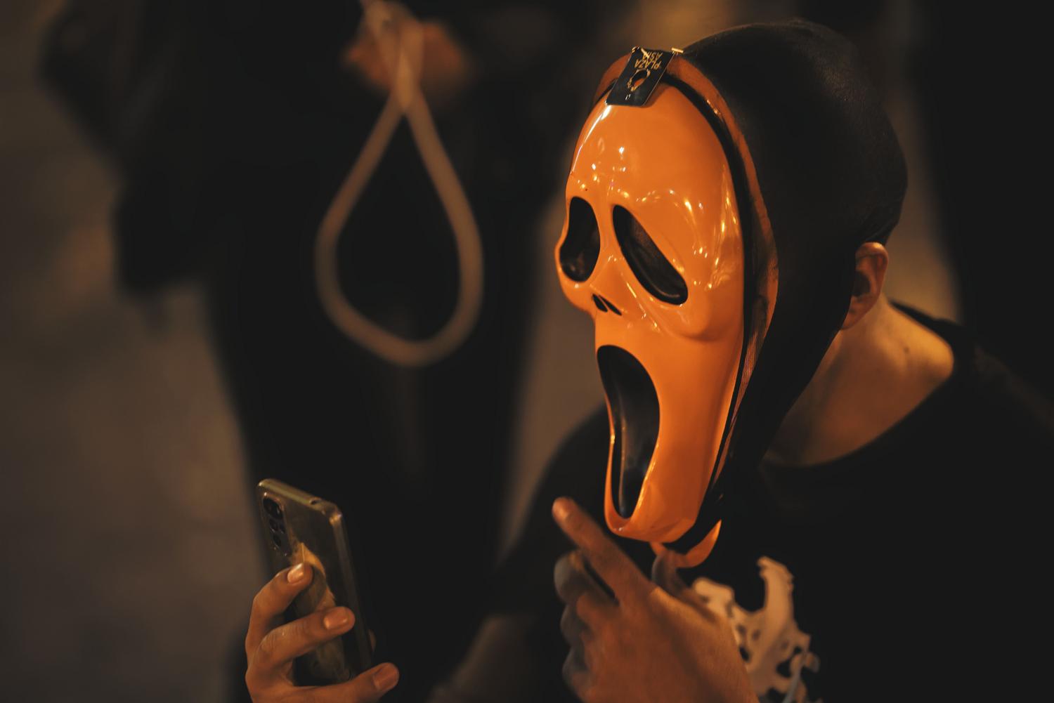 Persona con máscara de Halloween revisando su smartphone durante la noche, capturando una atmósfera misteriosa y tecnológica.
