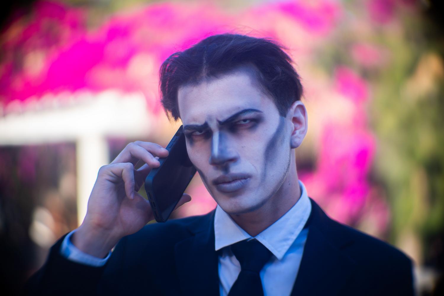 Hombre con maquillaje terrorífico de Halloween hablando por teléfono al aire libre, combinando la tecnología móvil con el espíritu festivo.