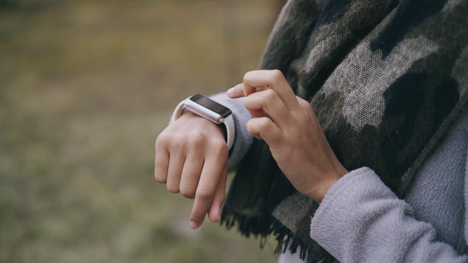 Persona revisando las notificaciones de su smartwatch en un entorno natural al aire libre.