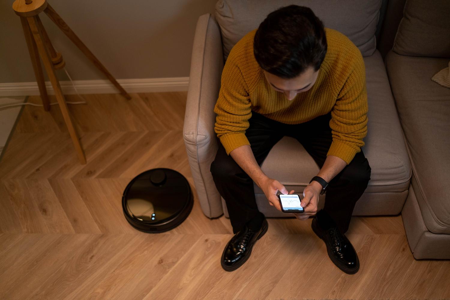 Hombre sentado en el sofá utilizando un smartphone para controlar los dispositivos de su hogar inteligente en un salón moderno.