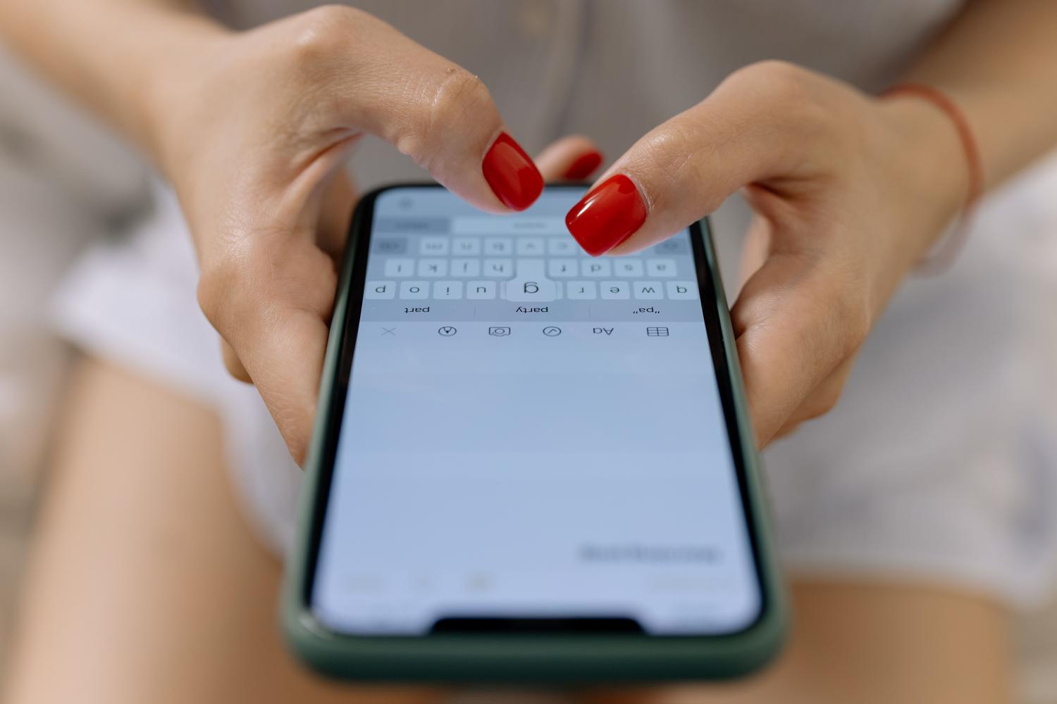 Manos escribiendo rápidamente un mensaje en la pantalla de un smartphone moderno.