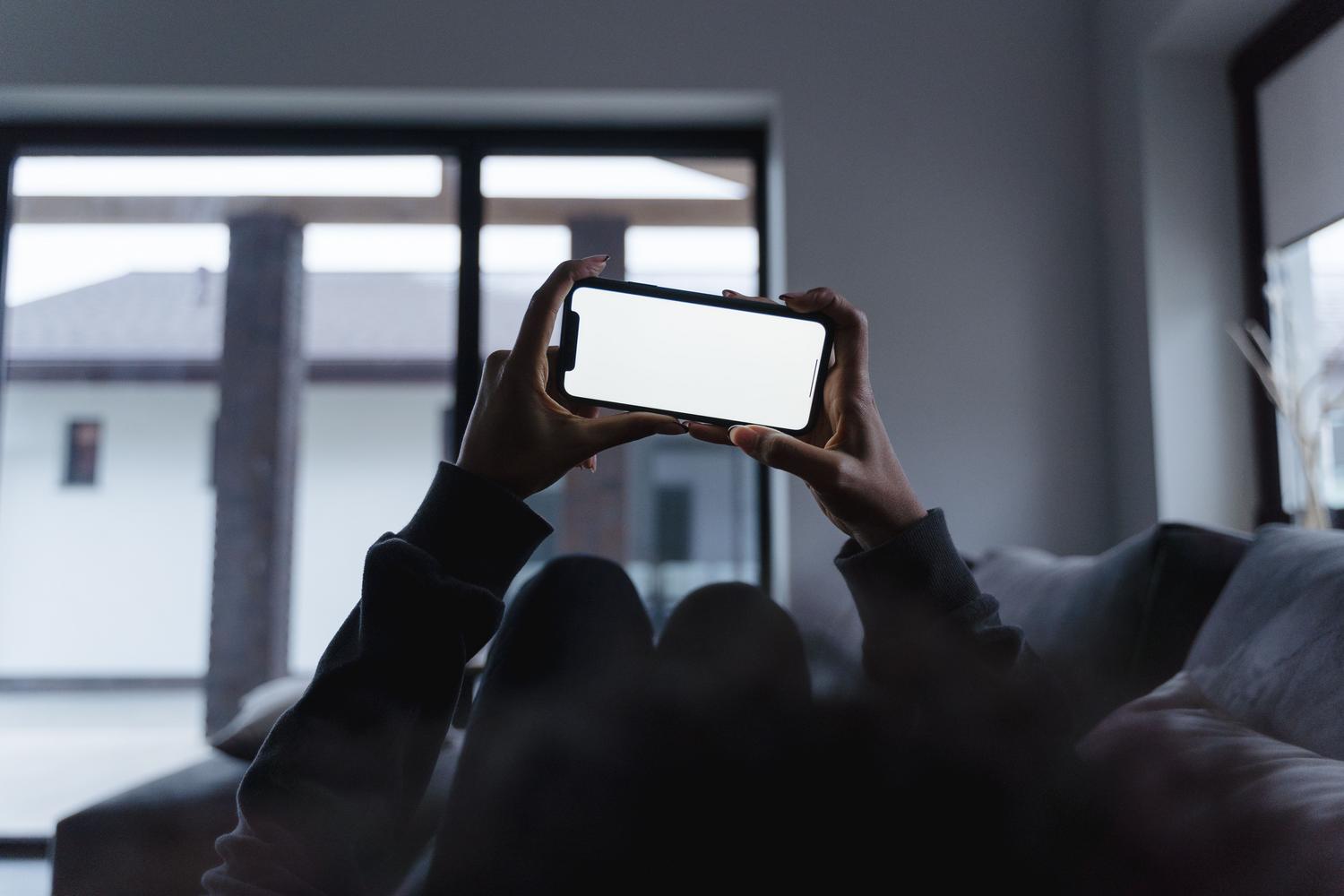 Persona usando un smartphone en posición horizontal mientras descansa en un sofá, representando la recepción de la transmisión de Meta Quest en el móvil.