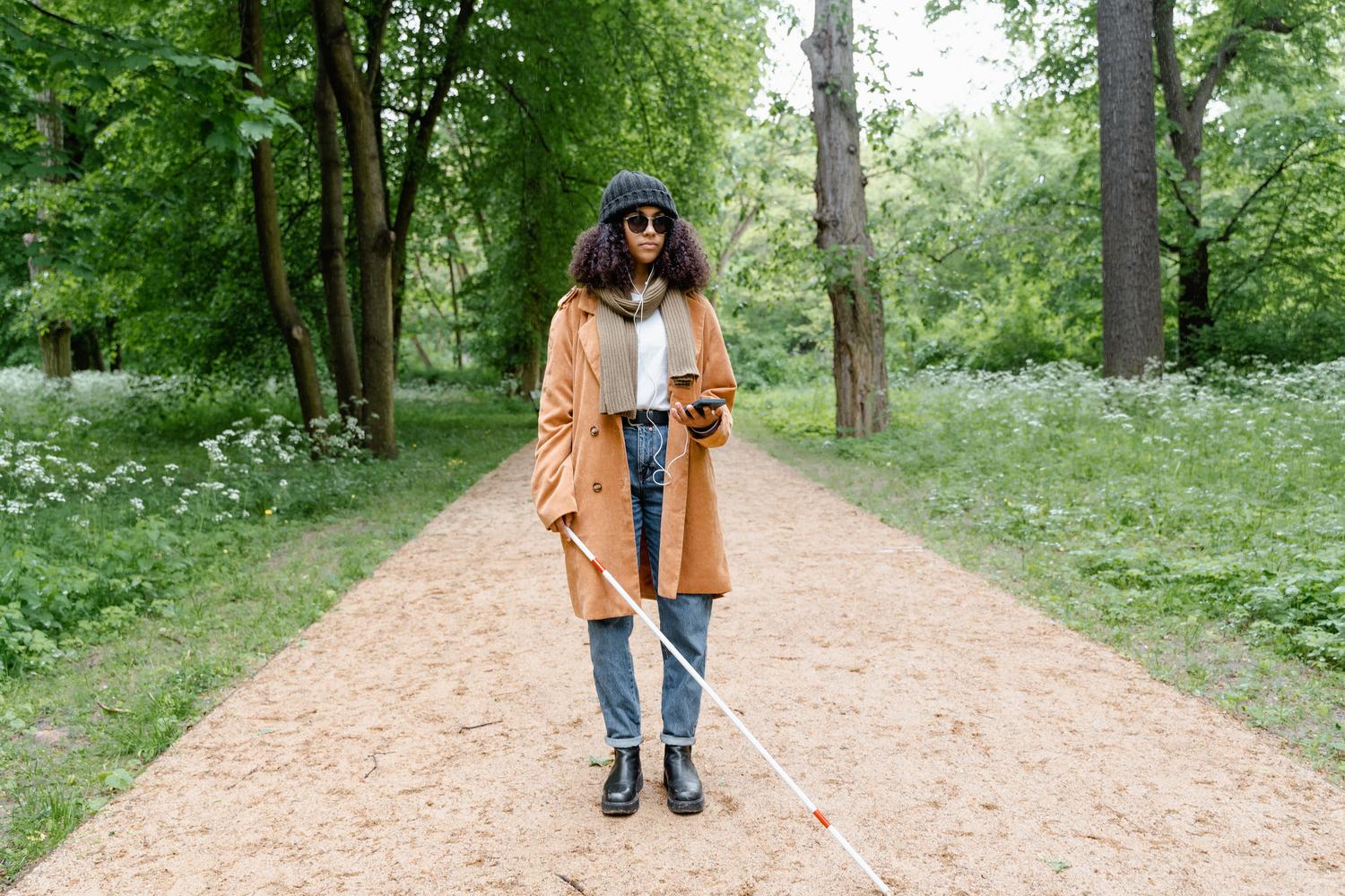 Mujer con discapacidad visual caminando por un parque mientras utiliza su smartphone con auriculares para escuchar el lector de pantalla.